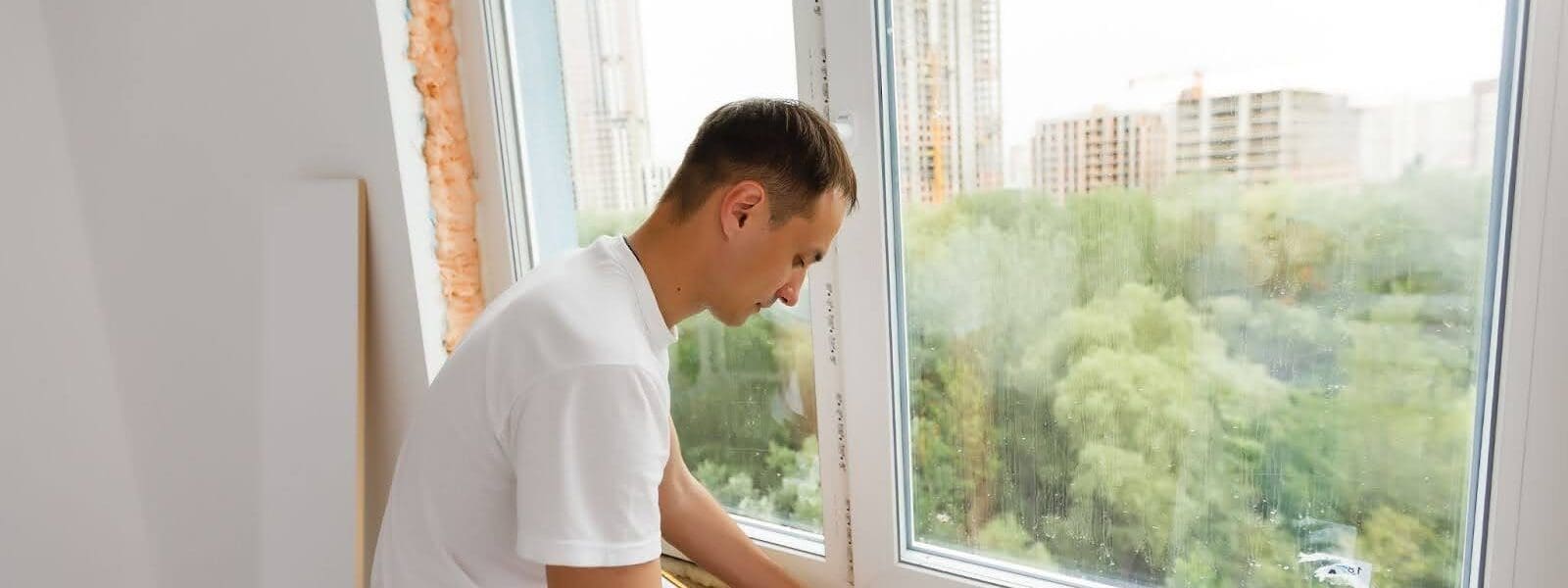 A man works on a window installation with a city view